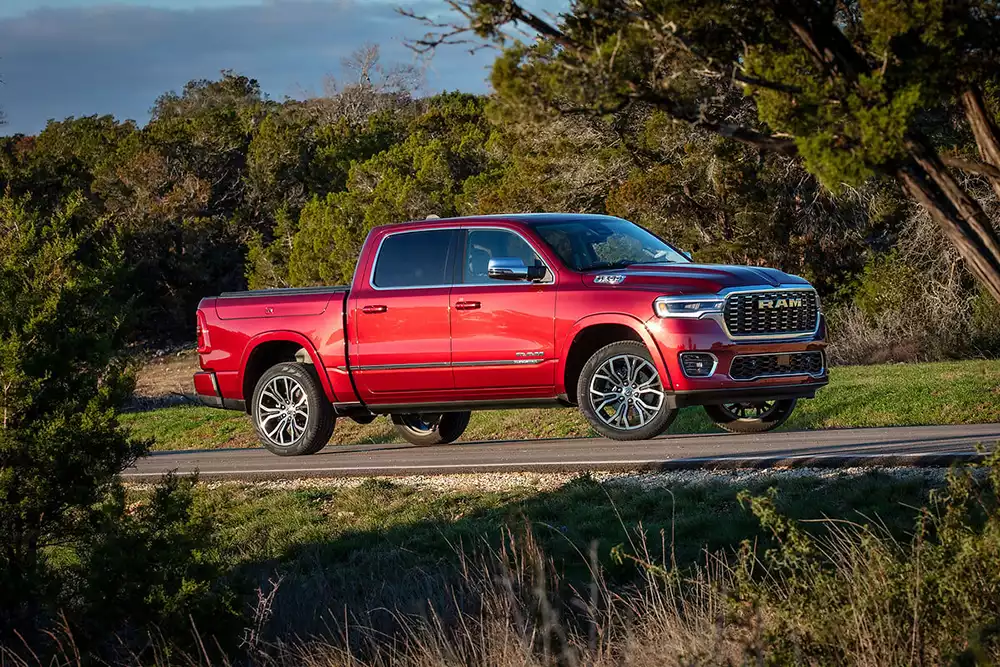 A red Ram 1500 Tungsten luxury pickup truck driving on a paved road with green trees in the background