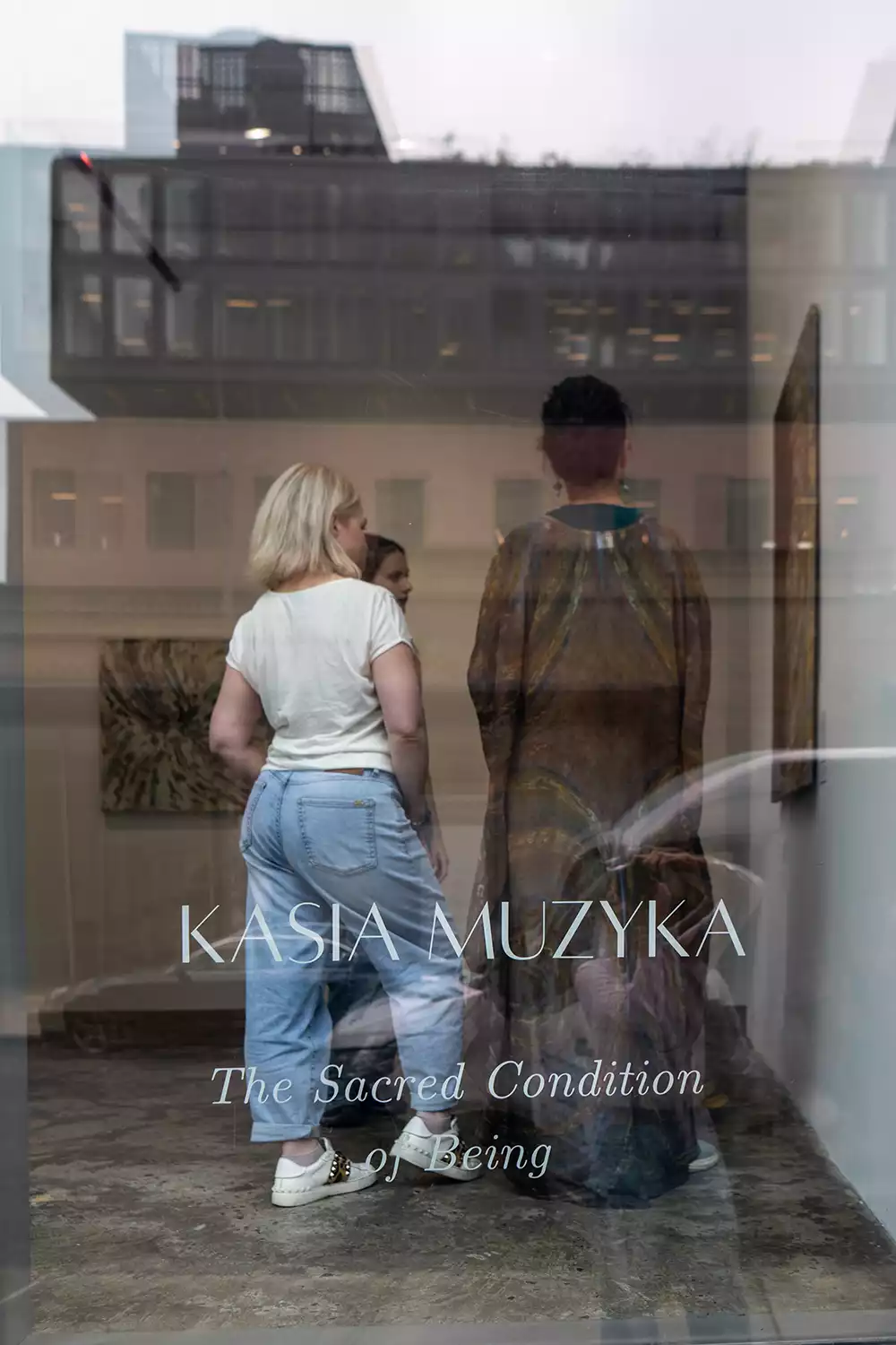 Inside the gallery, Kasia Muzyka’s presence is captured through a glass canvas etched with The Sacred Condition of Being, blended with ghostly city reflections.