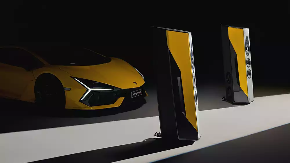 A yellow Lamborghini Revuelto beside a pair of Sonus faber Il Cremonese Ex3me Lamborghini edition loudspeakers in a matching yellow and black finish.
