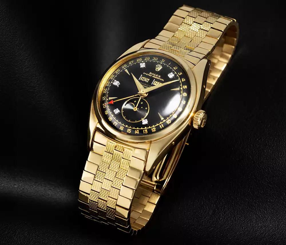 A yellow-gold Rolex 6062 with a black diamond dial and tile bracelet on a dark background