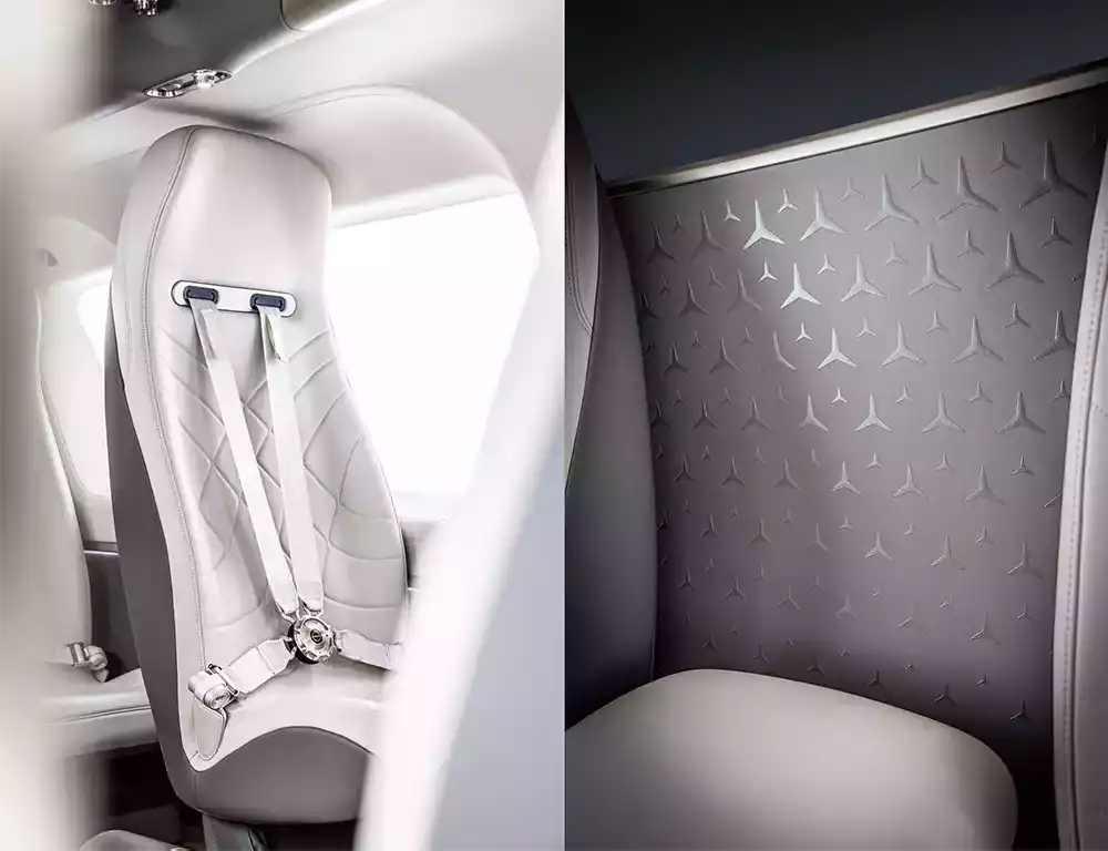 Close-up of white leather quilted seats with seatbelts and a wall panel featuring the iconic Mercedes-Benz star pattern inside the ACH145 helicopter